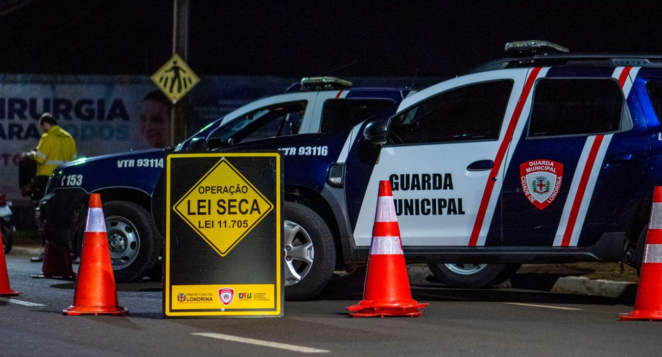 Viaturas da Guarda Municipal e cones em um bloqueio policial noturno em uma rua de Londrina, no Brasil.