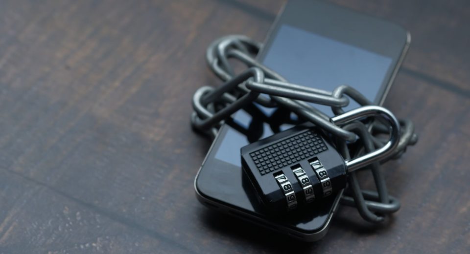 Close de um celular envolto por uma corrente com cadeado, simbolizando restrição e segurança.