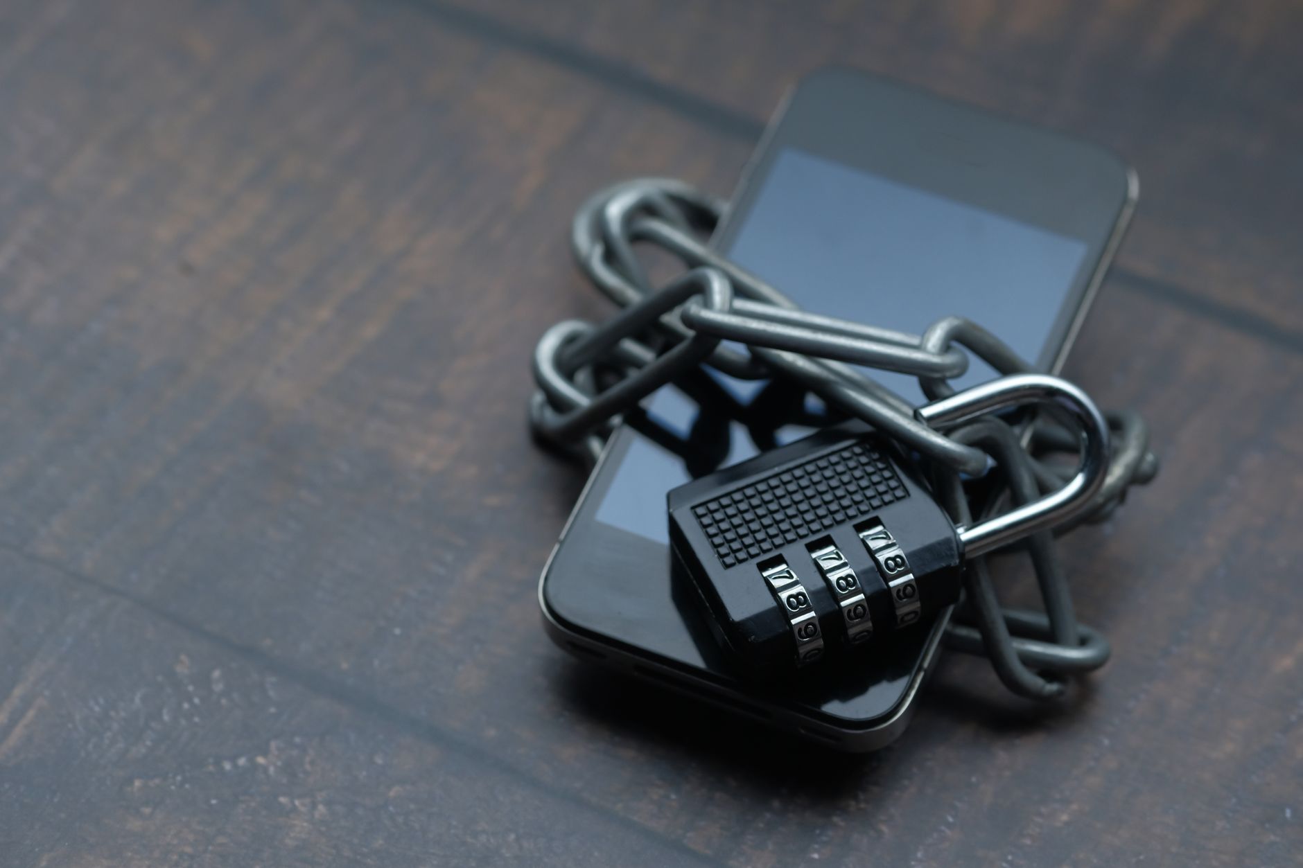 Close de um celular envolto por uma corrente com cadeado, simbolizando restrição e segurança.