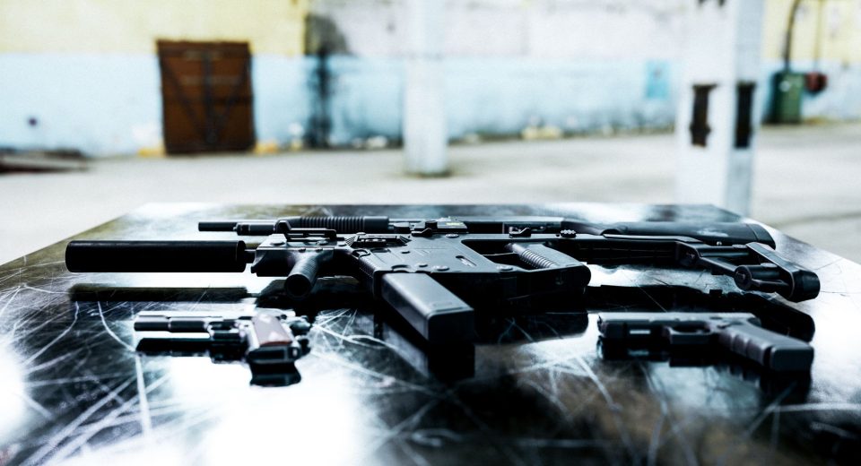 Diversas armas de fogo expostas sobre uma mesa metálica em ambiente industrial