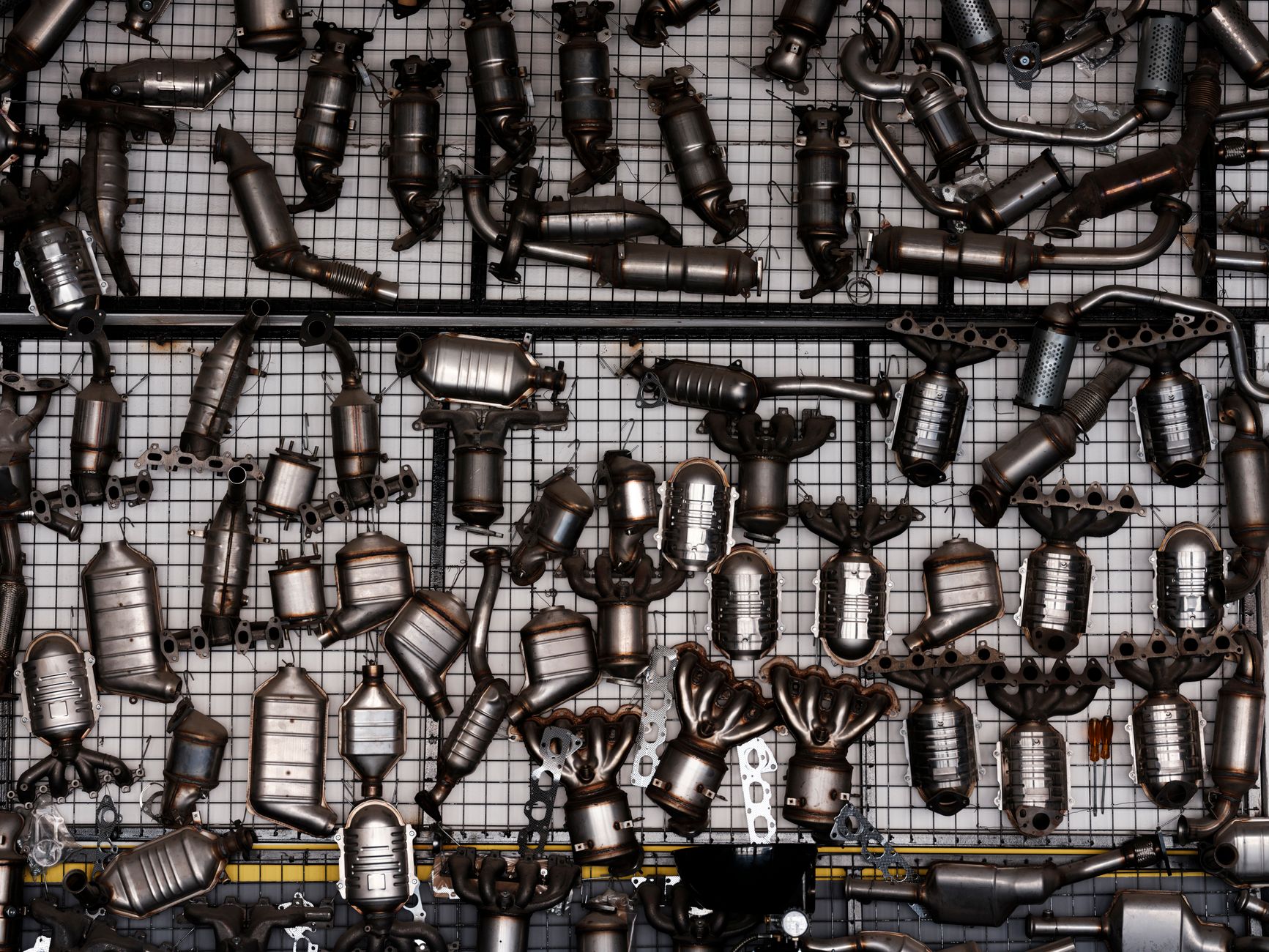 Diversas peças de escapamento automotivo expostas em uma parede de uma garagem industrial