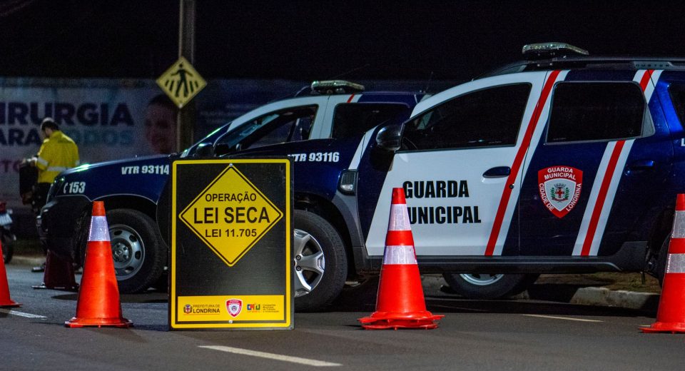 Viaturas da Guarda Municipal e cones em um bloqueio policial noturno em uma rua de Londrina, no Brasil.