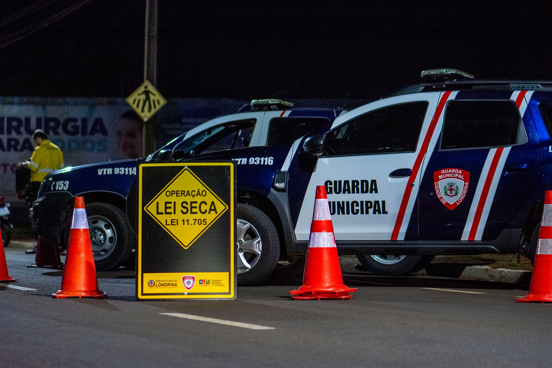 Viaturas da Guarda Municipal e cones em um bloqueio policial noturno em uma rua de Londrina, no Brasil.