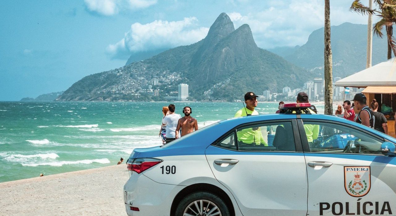 Viatura policial circula à beira da praia de Ipanema, no Rio de Janeiro, com os Dois Irmãos ao fundo.