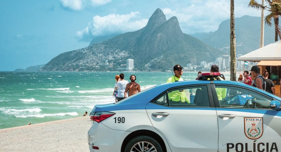 Viatura policial circula à beira da praia de Ipanema, no Rio de Janeiro, com os Dois Irmãos ao fundo.