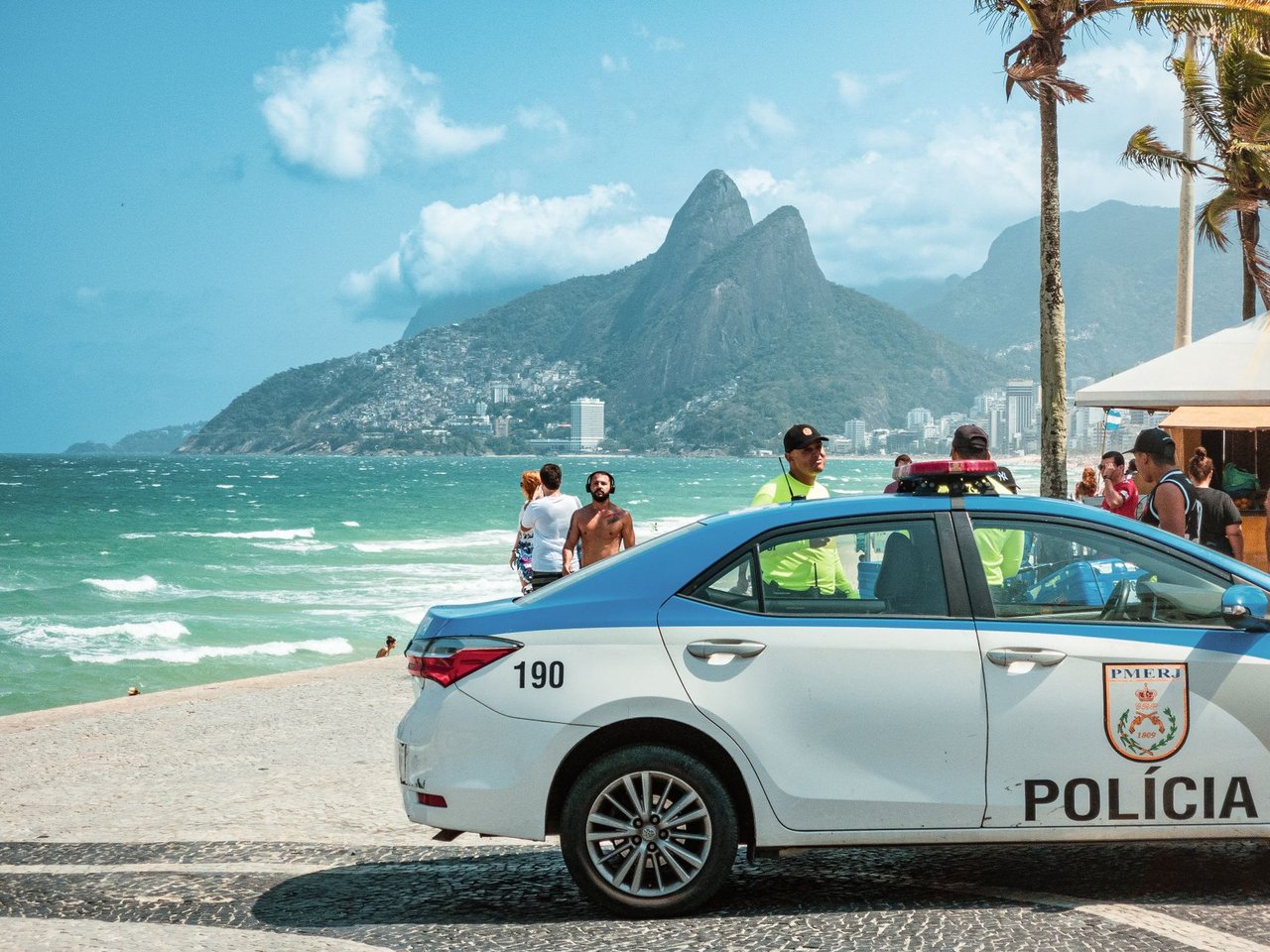 Viatura policial circula à beira da praia de Ipanema, no Rio de Janeiro, com os Dois Irmãos ao fundo.