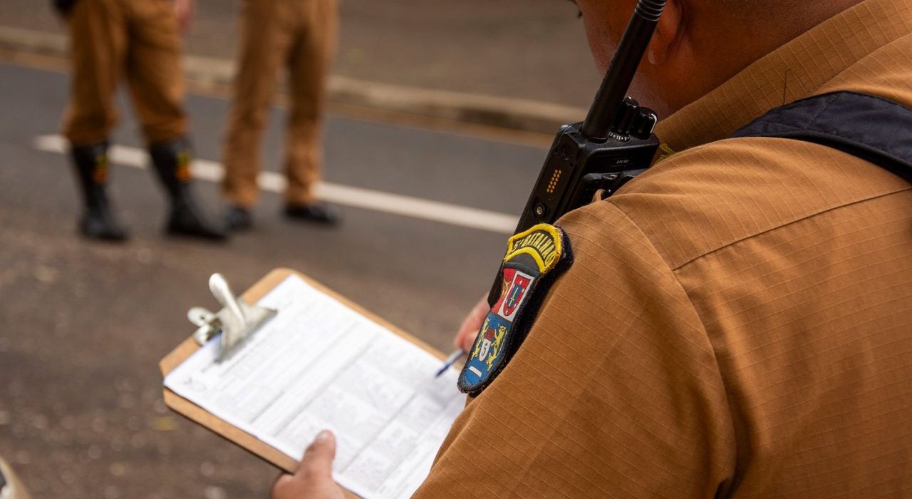 Policial faz anotações em uma prancheta durante uma atividade externa.