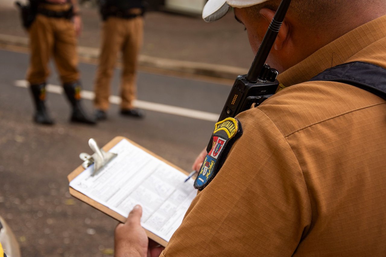 Policial faz anotações em uma prancheta durante uma atividade externa.
