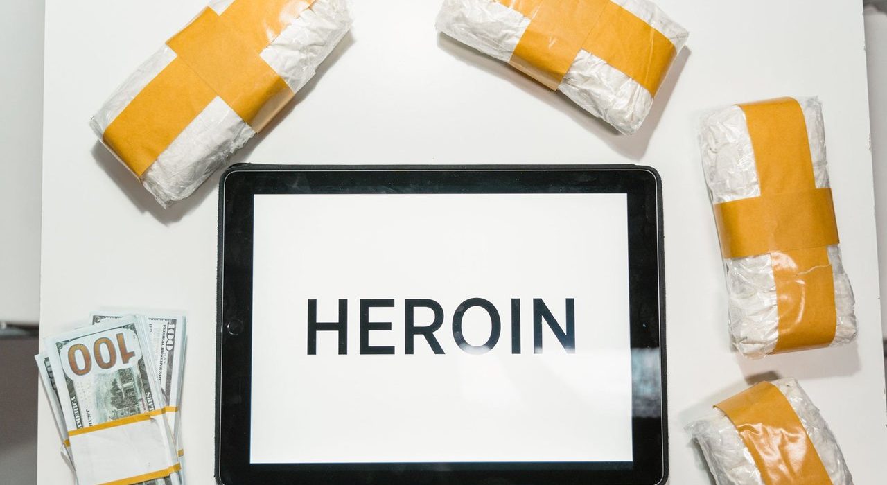 Embalagens de drogas, dinheiro e um tablet dispostos sobre uma superfície escura.