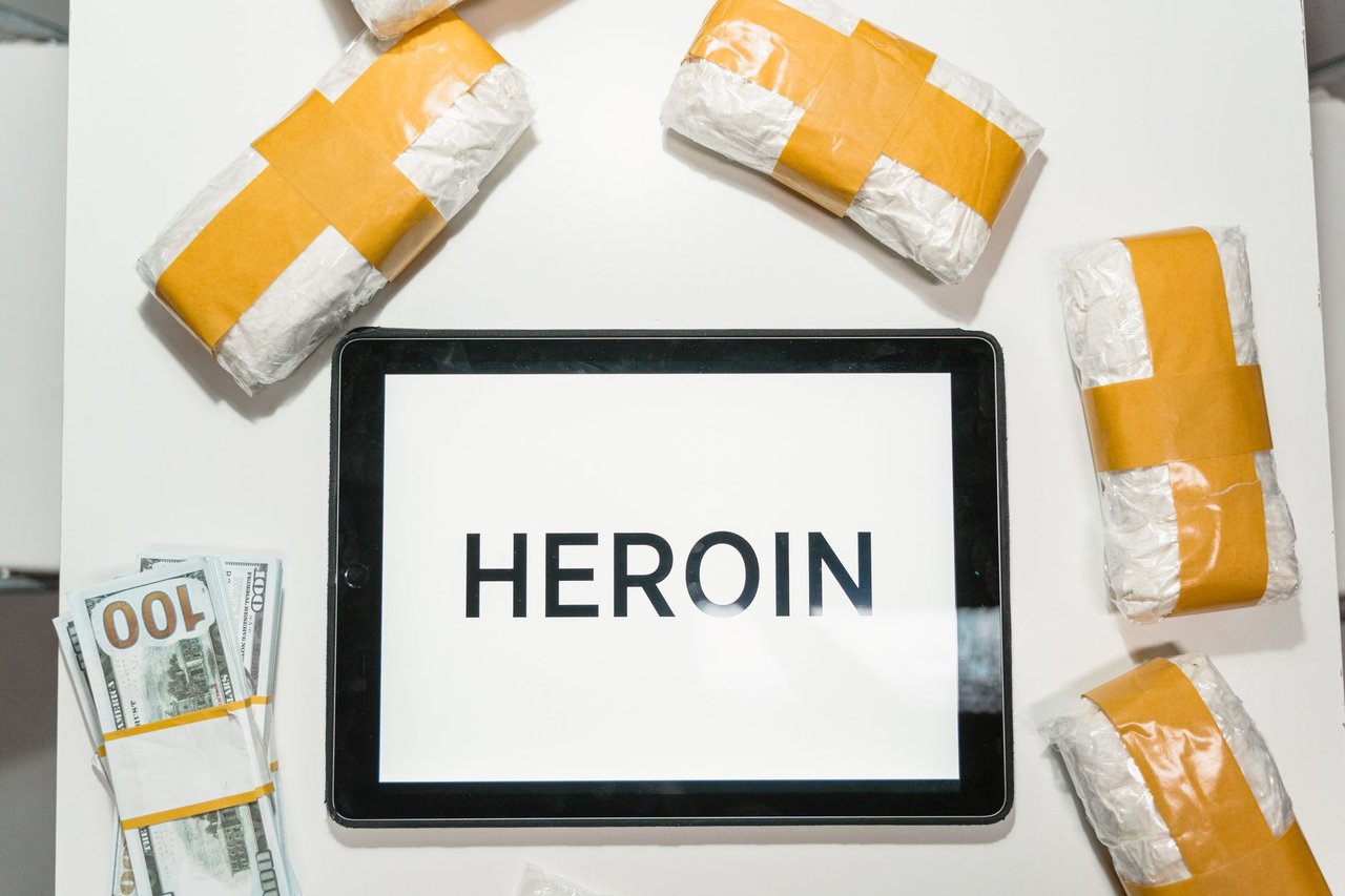 Embalagens de drogas, dinheiro e um tablet dispostos sobre uma superfície escura.