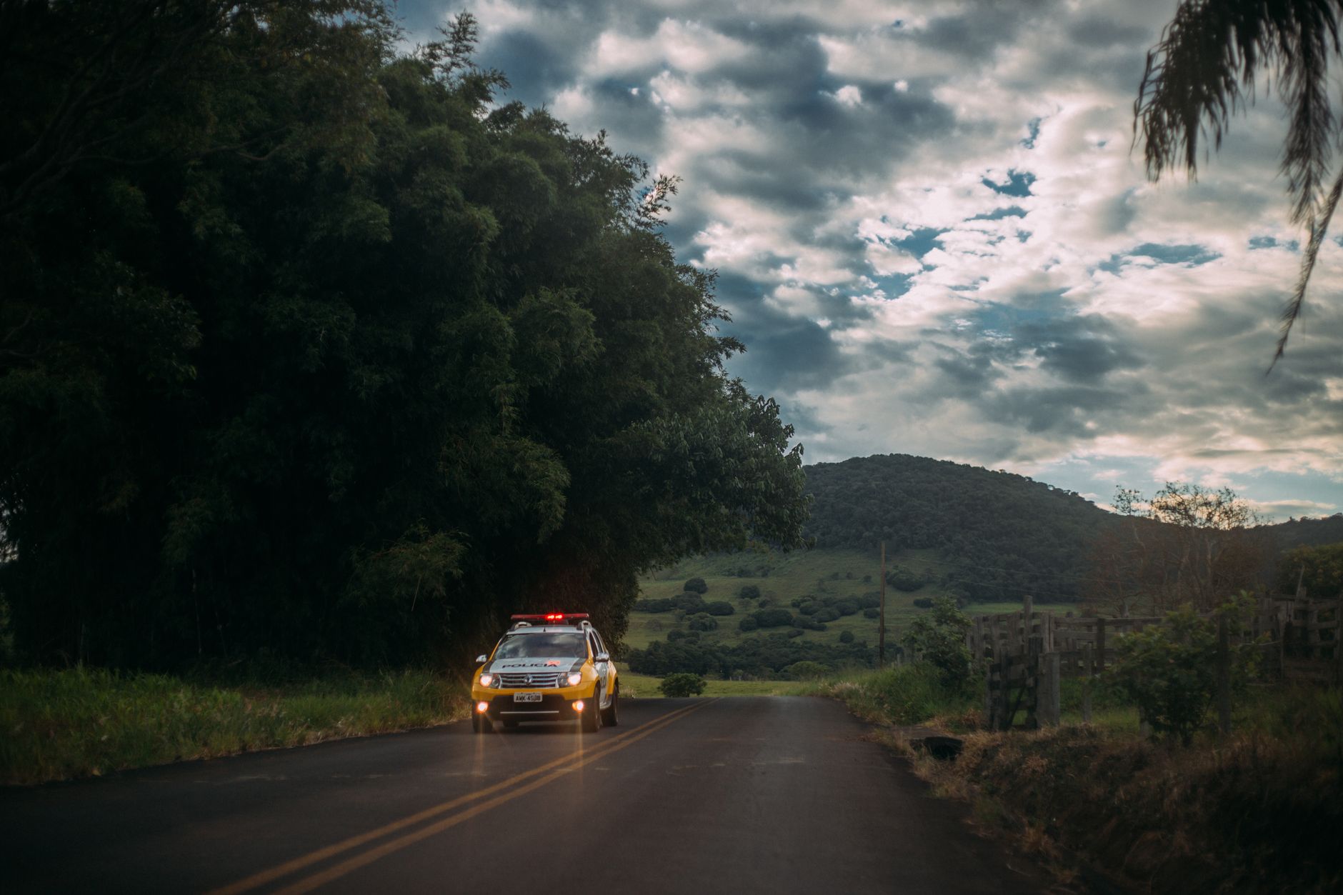 Viatura policial percorre uma estrada rural ao entardecer.