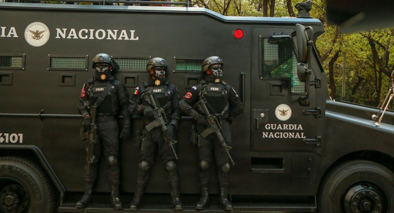 Agentes de segurança em trajes táticos ao lado de um veículo blindado durante uma operação.