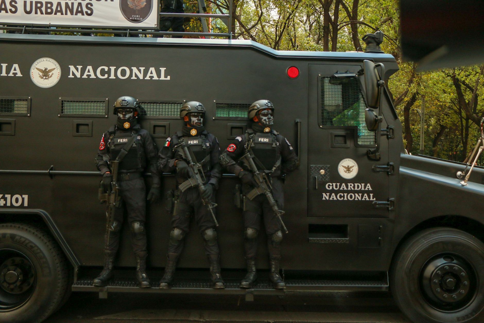 Agentes de segurança em trajes táticos ao lado de um veículo blindado durante uma operação.